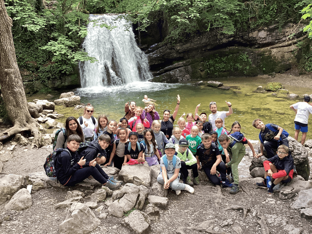 Cheadle Hulme Primary School pupils from Year 4 stand in front of a scenic waterfall in Malham.